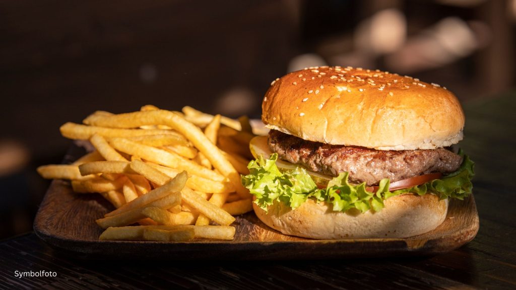 Saftiger Burger mit gegrilltem Rindfleisch-Patty, frischem Salat, Tomaten und Zwiebeln auf einem Sesam-Brioche-Bun, serviert mit goldenen Pommes Frites auf einem rustikalen Holzbrett